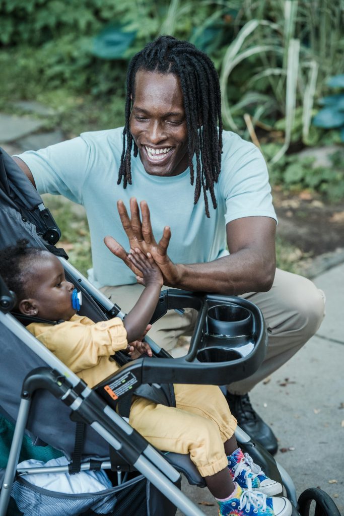 Un père et son enfant en poussette se tapent dans la main avec le sourire, contents de partager un moment ensemble.