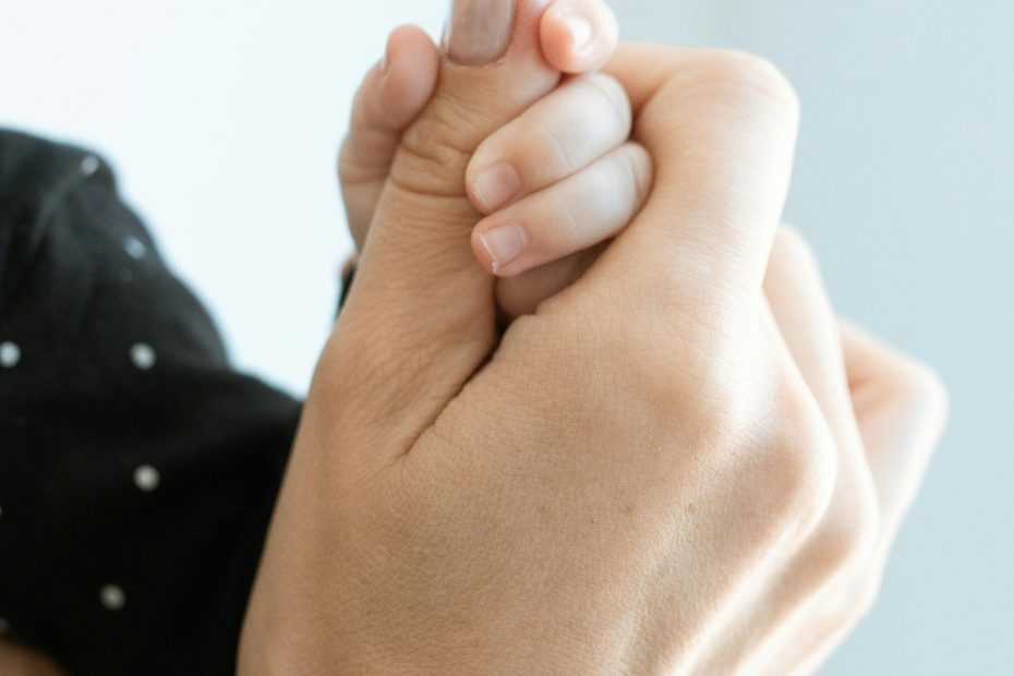 Une main d'adulte tient une main de bébé, en gros plan.