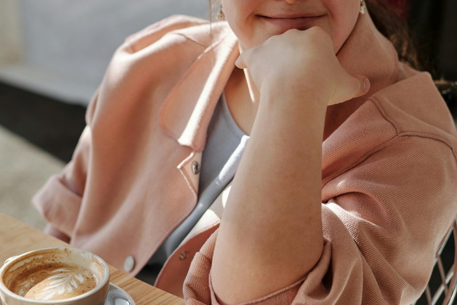 Jeune femme porteuse de trisomie 21 souriant, assise à une table, une main devant sa bouche.